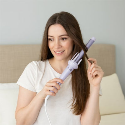 une femme souriante utilise un boucleur automatique 